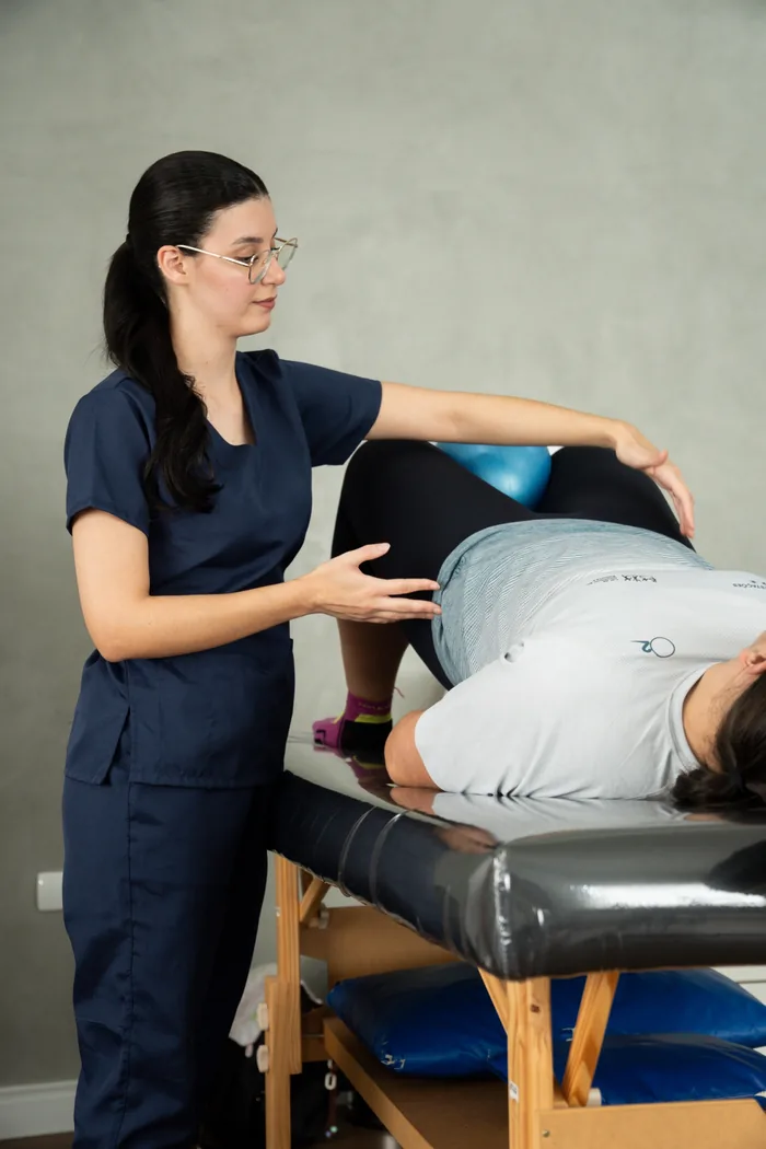 Natália orientando um exercício de ponte com bola em uma paciente deitada na maca